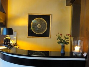 Un mostrador de recepción con una obra de arte enmarco, un florero con flores y una vela encendida en la encimera.