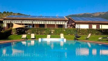 Ein Swimmingpool mit Liegestühlen, eine überdachte Terrasse und Solaranlagen auf dem Dach.