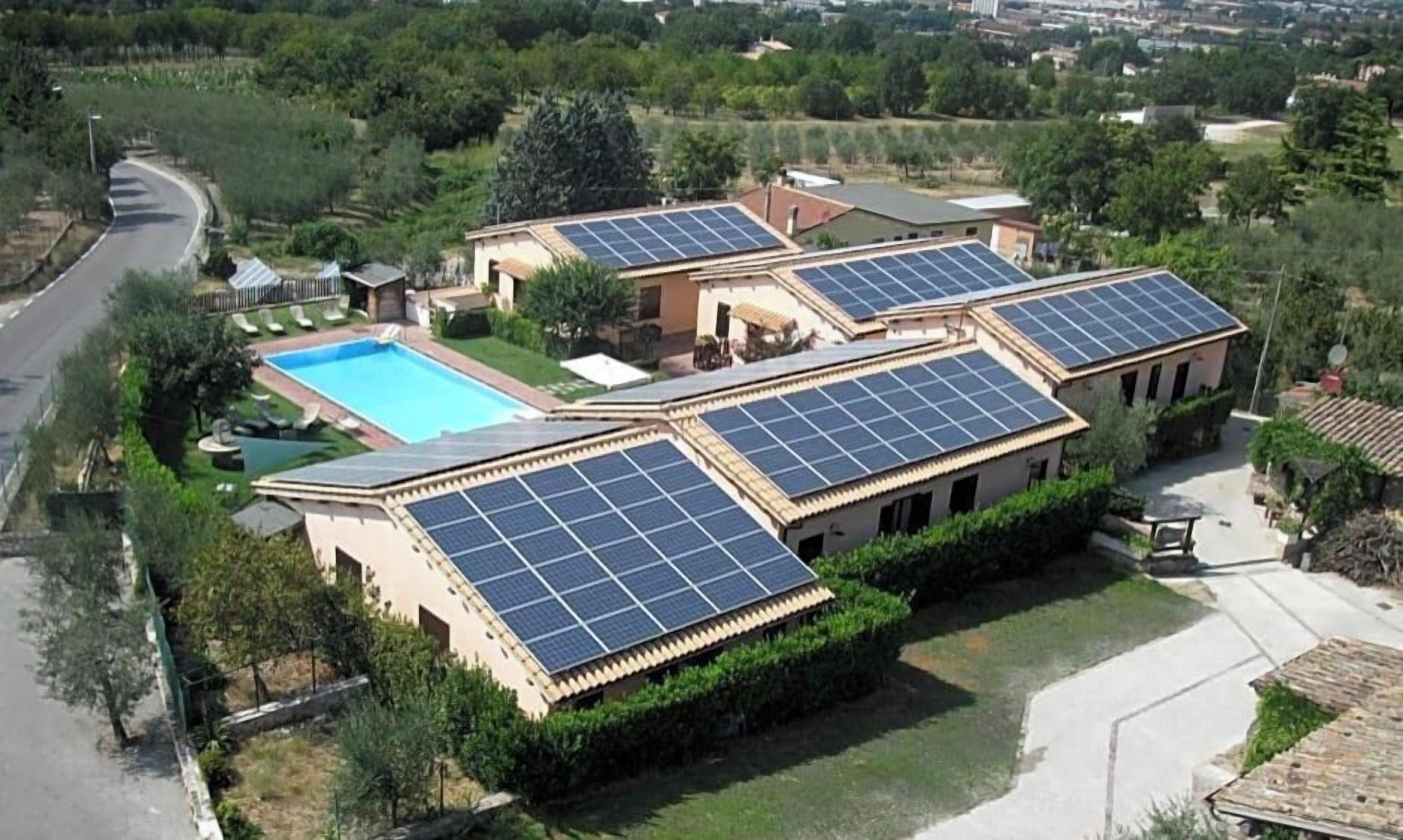 Ein Wohnhaus mit mehreren Solaranlagen auf den Dächern, einem Schwimmbad und einem gepflegten Garten.