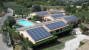 Ein Wohnhaus mit mehreren Solaranlagen auf den Dächern, einem Schwimmbad und einem gepflegten Garten.