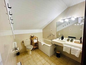 Une salle de bain avec des toilettes, une baignoire et un grand miroir.