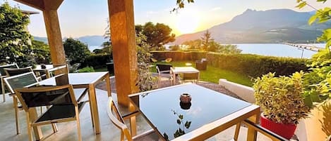 Un espacio al aire libre con mesas y sillas, con vista a un cuerpo de agua y montañas.