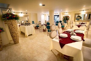 A banquet hall with multiple tables set for dining, featuring white tablecloths and red centerpieces. - Hotel Trugo (Armenia)