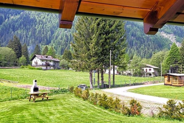 Une vue d’une zone rurale avec une structure en bois, une table de pique-nique dotée d’un barbecue et des maisons en arrière-plan.
