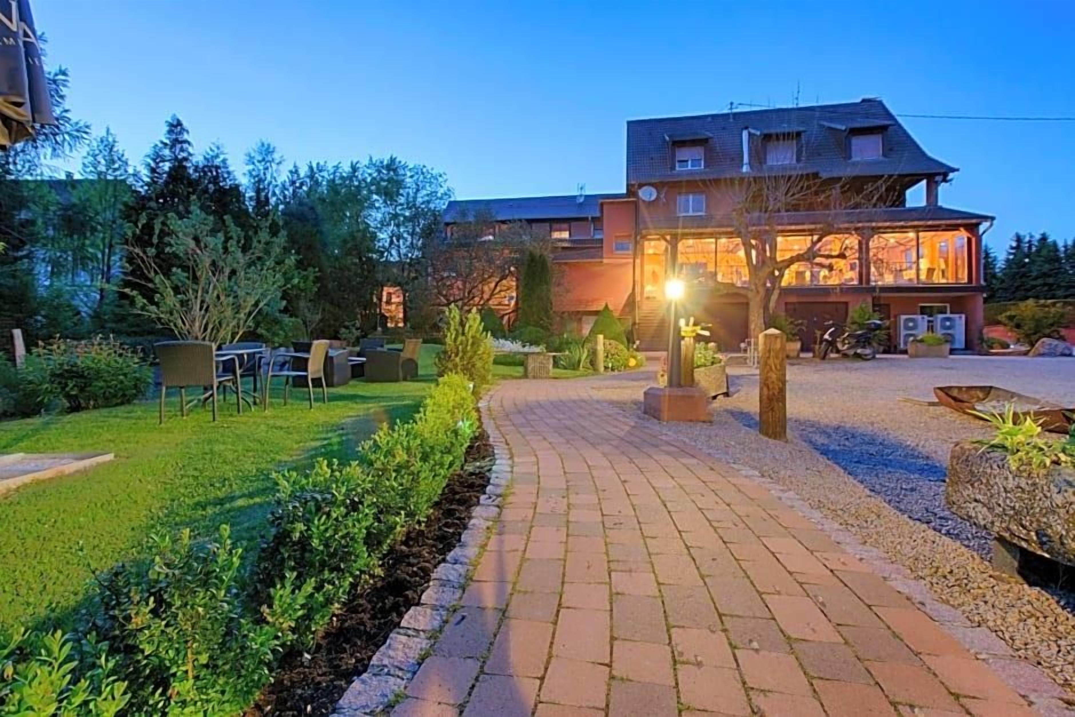 A hotel with a paved driveway leading to a building with multiple windows and a well-maintained garden.