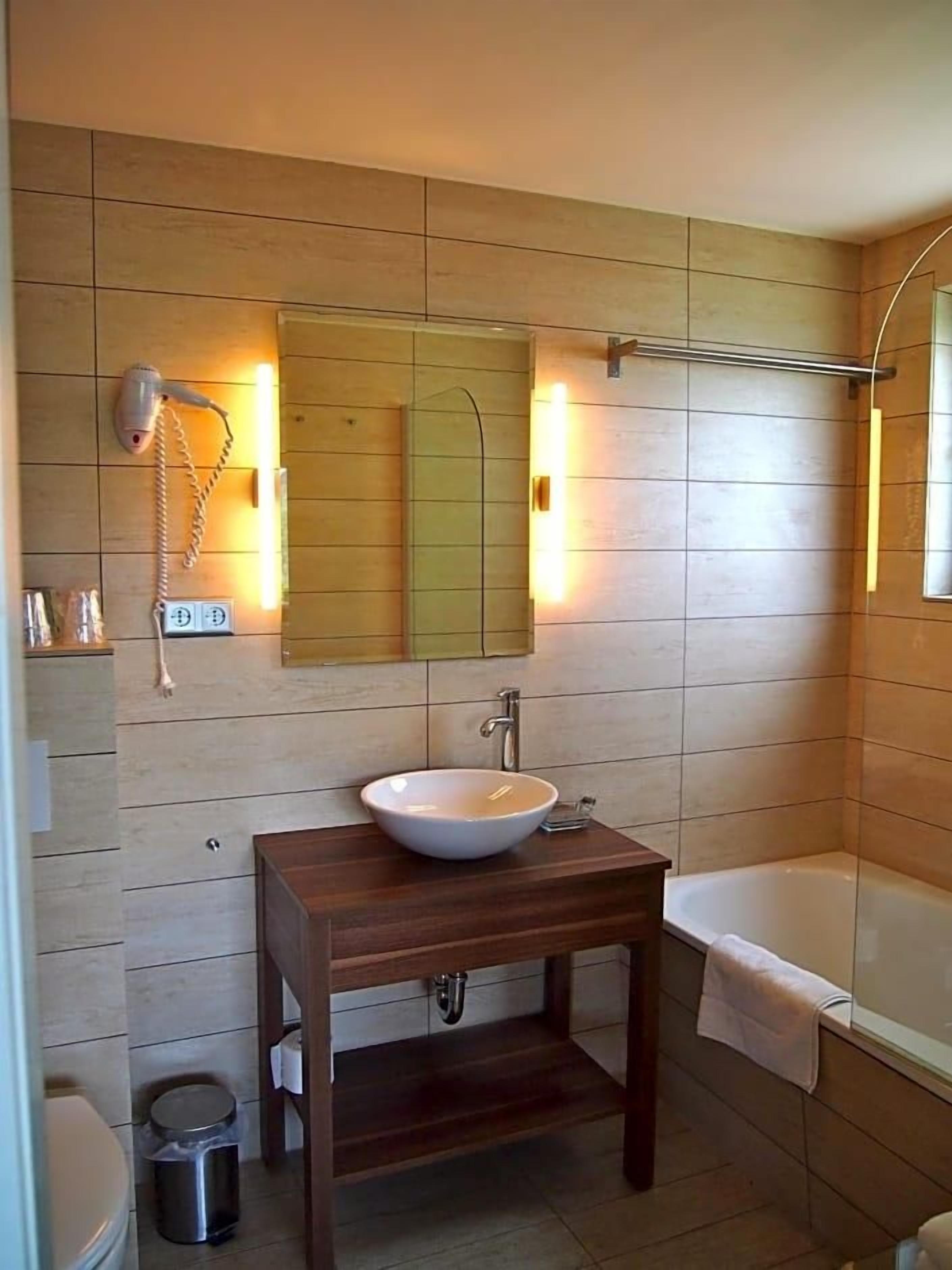 Een badkamer met een houten wastafelmeubel, een witte wastafel, een spiegel, een handdoekhouder en een douche.