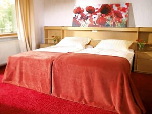 Una habitación de hotel con una cama, un cuadro en la pared y un ventanal con cortinas.