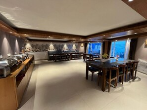A spacious dining area with a long wooden table and chairs, a buffet counter with food items, and a seating area with sofas and a decorative wall mural. - The Retreat (Puri)