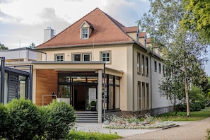 Un bâtiment à deux étages, doté d’un toit en pente, d’une entrée abritée et d’un jardin aménagé.