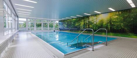 An indoor swimming pool with clear glass walls, a tiled floor, and a mural of a forest.