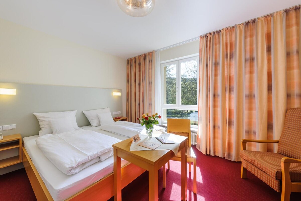 A hotel room with two beds, a desk, a chair, and a window with curtains.