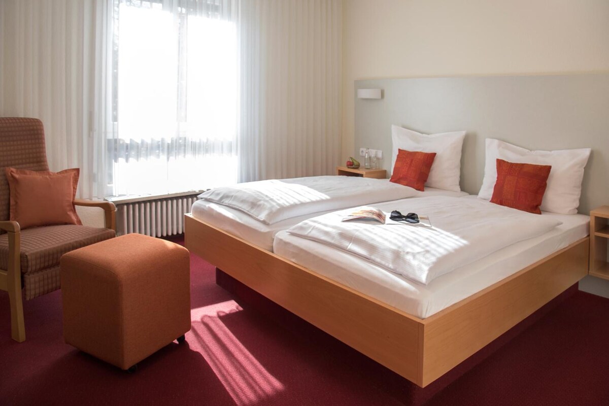 Une chambre d’hôtel avec un lit double, une chaise, une petite table et un radiateur.
