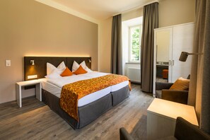 A hotel room with a bed, bedside tables, a desk, a chair, a wardrobe, and a window with curtains. - Hotel Kurhaus Bad Bocklet (Bad Bocklet)