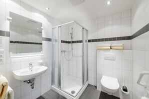 A modern bathroom with a glass-enclosed shower, a sink with a mirror, and a toilet. - Hotel Kurhaus Bad Bocklet (Bad Bocklet)