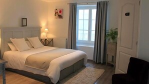 Un dormitorio con cama, mesitas de noche, una ventana con cortinas, una planta y una puerta.