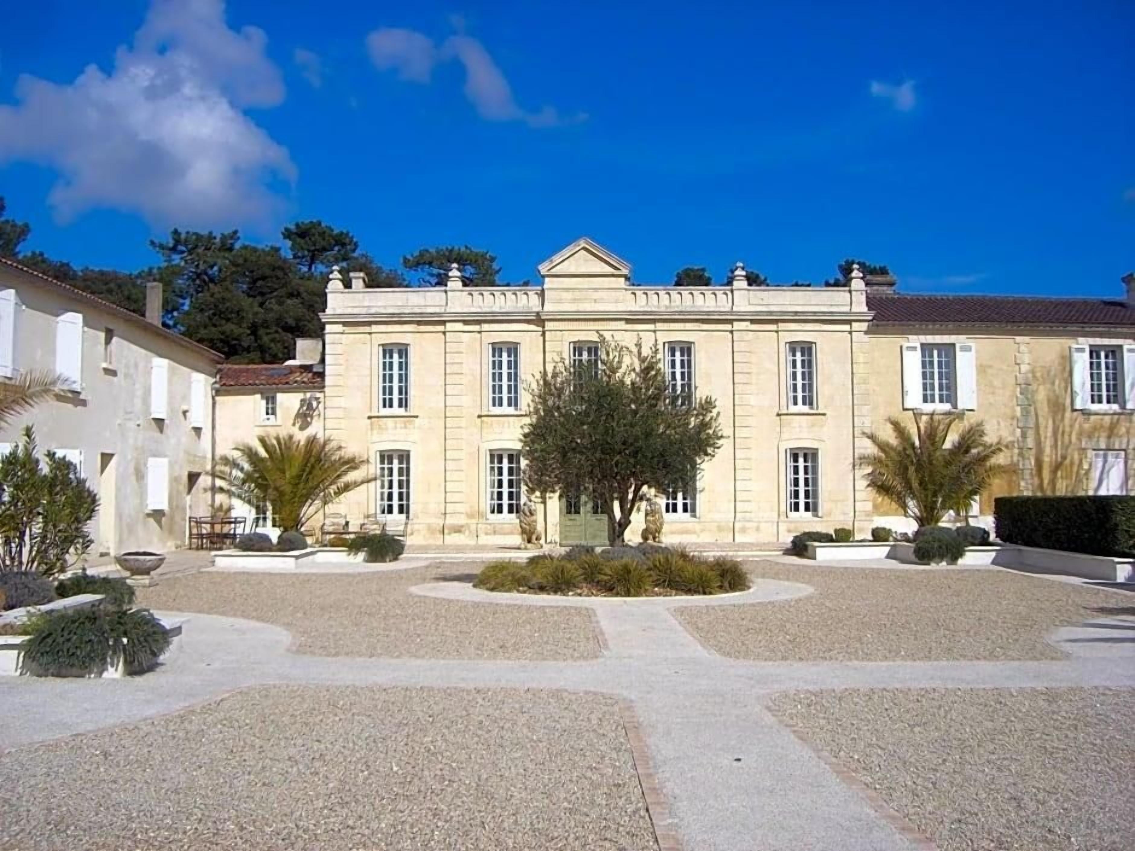 A large, classical building with a symmetrical facade, a central entrance, and a formal garden with gravel paths and trimmed hedges.