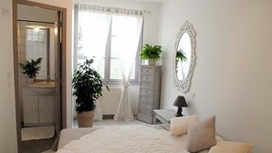 A bedroom with a bed, a dresser, a mirror, and two potted plants.