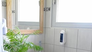 A bathroom with a wooden vanity, a white sink, a potted plant, and a mirror.