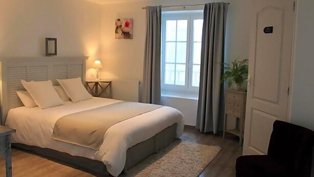 A bedroom with a bed, bedside tables, a window with curtains, a plant, and a door.
