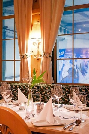 Mesa de comedor para cuatro, con un florero, una lámpara de pared encendida y vista a un paisaje nevado a través de una ventana.
