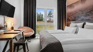 Habitación de hotel con cama, escritorio con silla, televisión y un ventanal con vistas a árboles y un paisaje.
