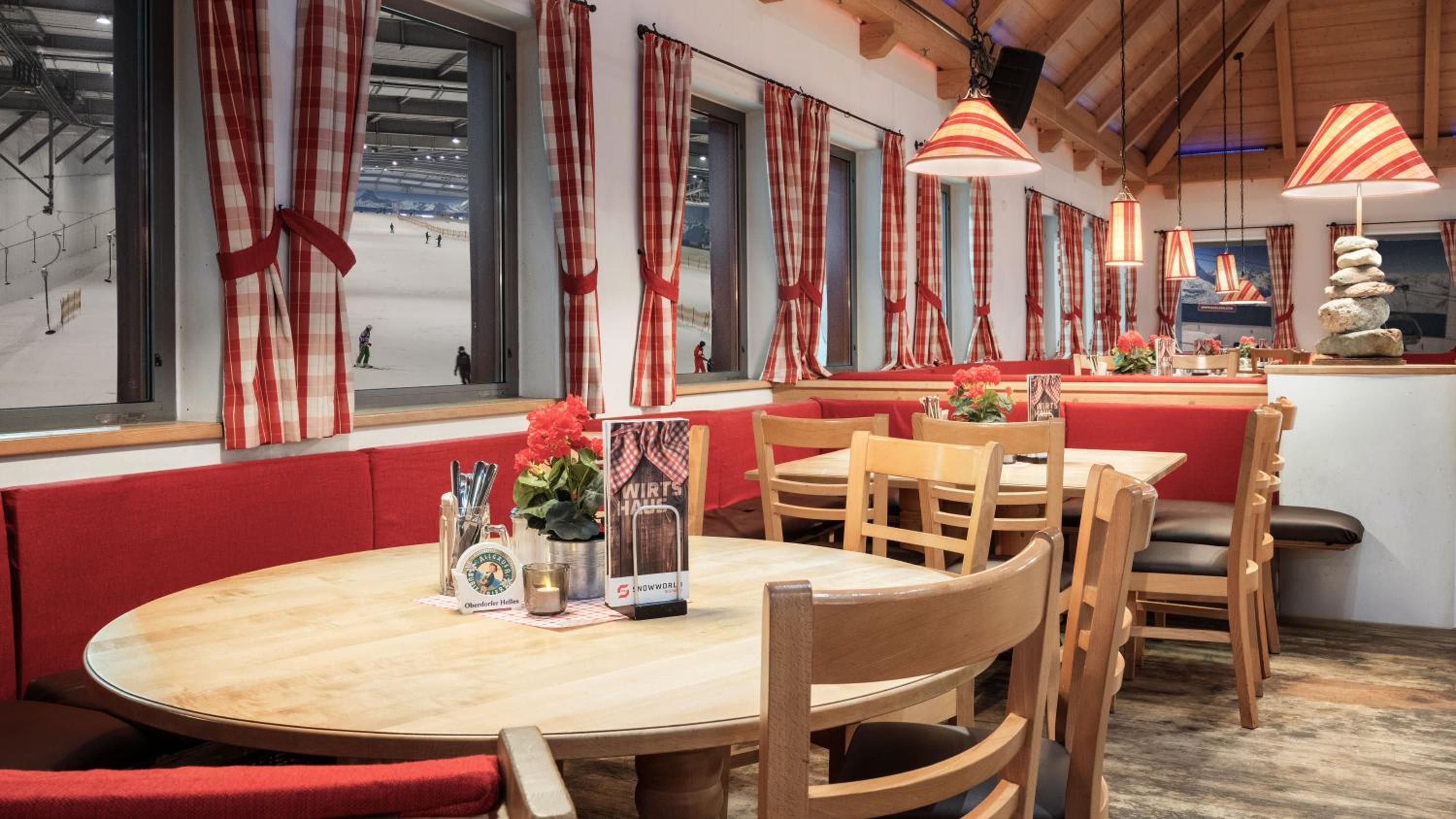 Ein Restaurant mit Holztischen, roten Kissen und Blick auf einen Außenbereich.