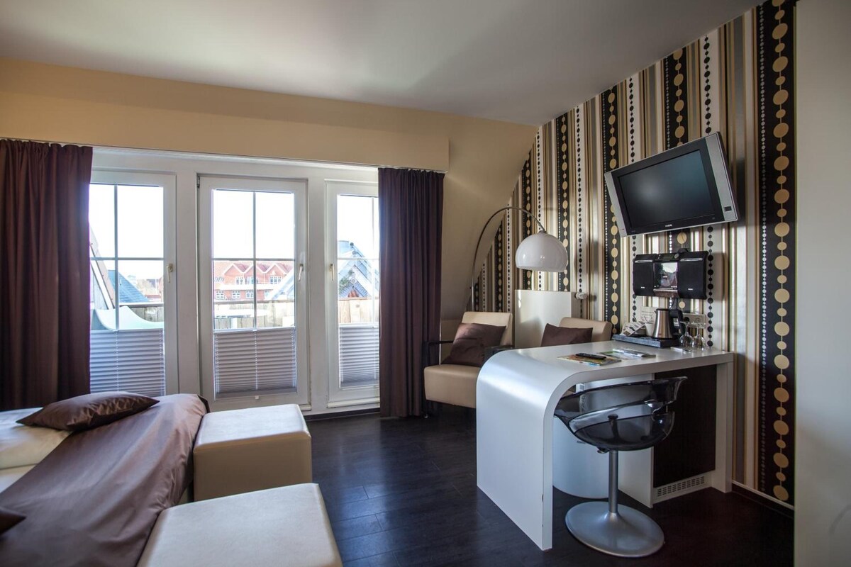 Habitación de hotel con cama, escritorio con silla, televisor y vista a un edificio a través de una ventana.