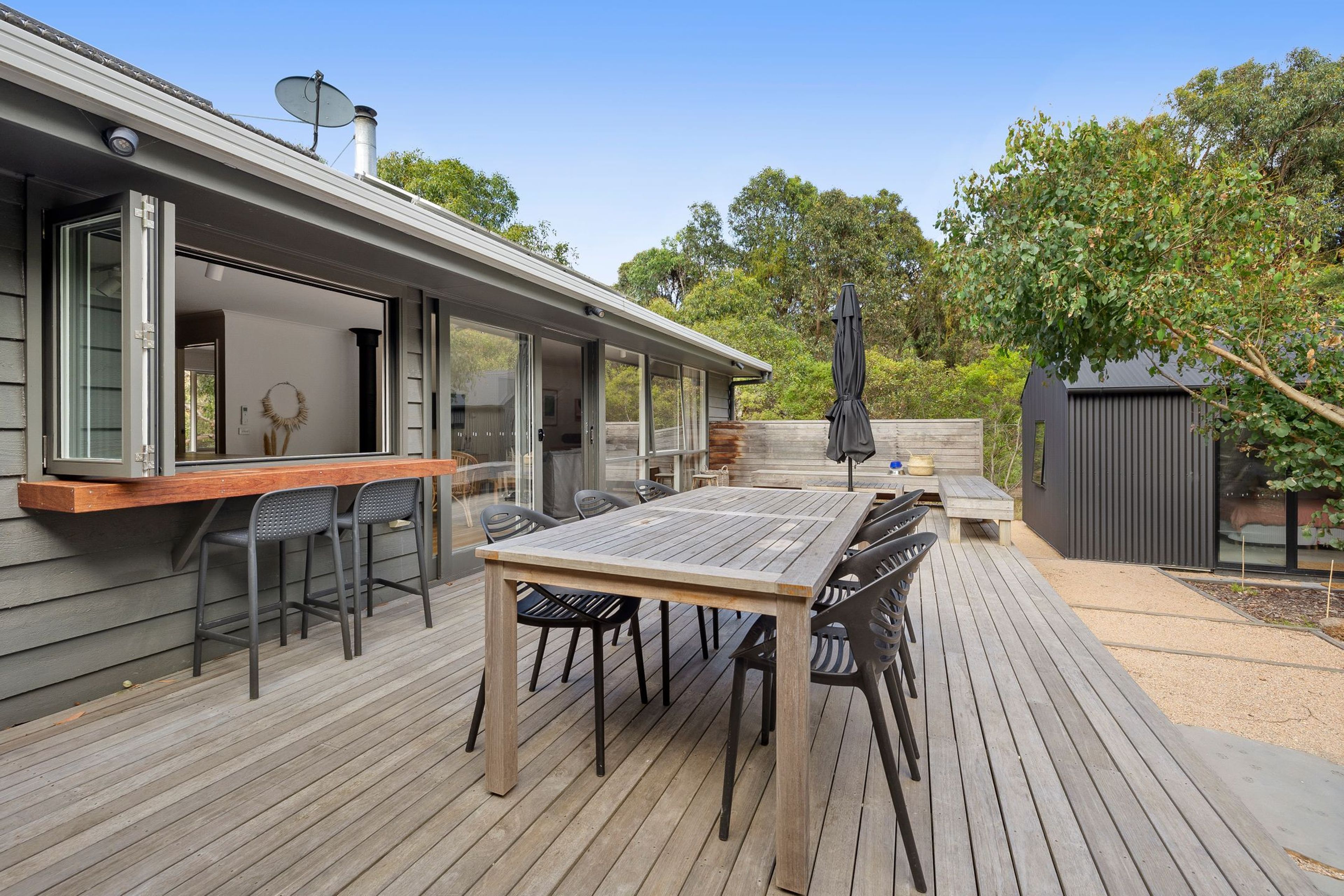 A deck with a wooden table and chairs, a barbecue grill, and a covered outdoor area with a patio umbrella.