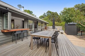 Eine Terrasse mit Holztisch und -stühlen, einem Grill und einem überdachten Bereich mit Sonnenschirm.