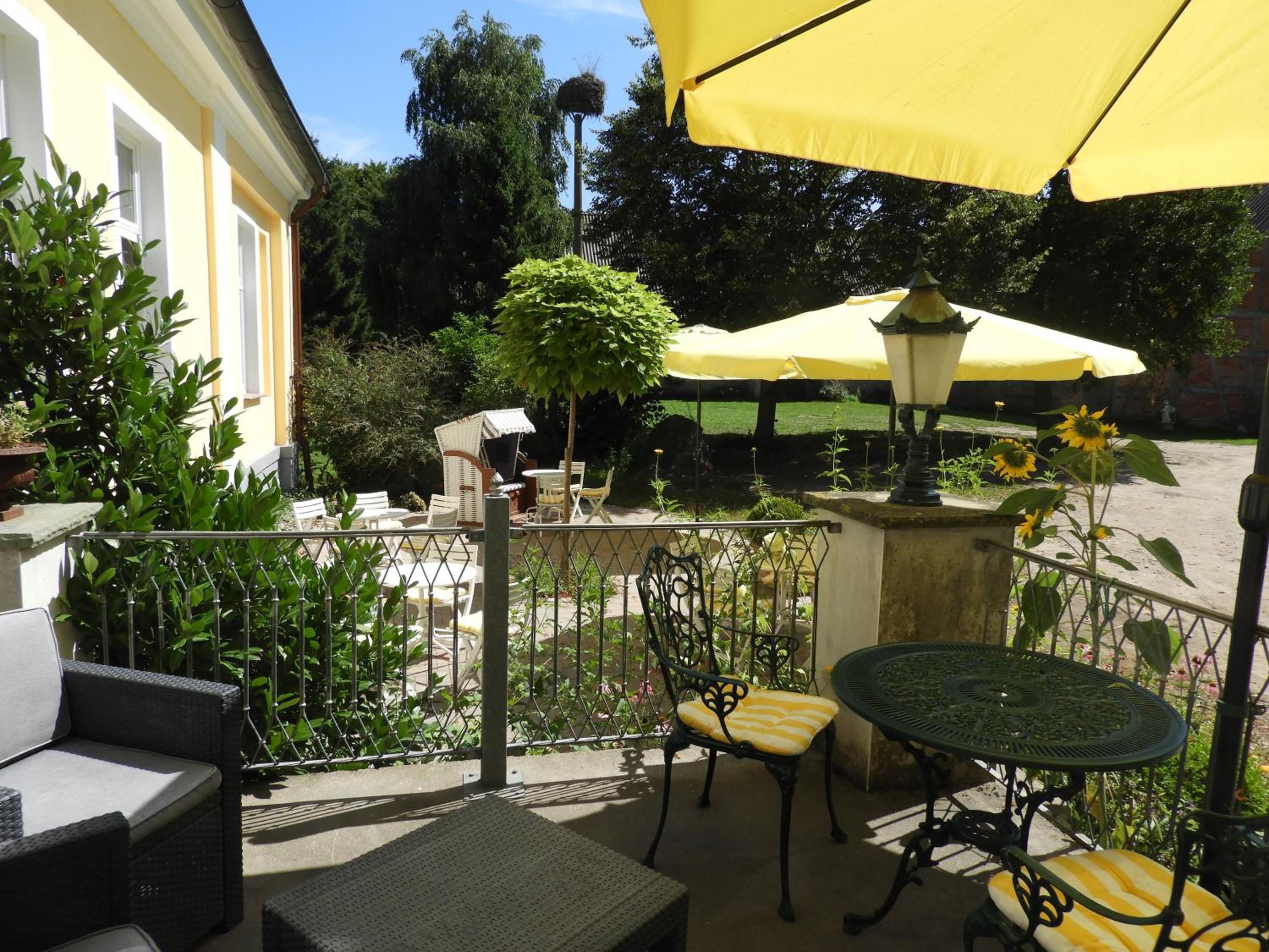 An outdoor patio with a table and chairs, surrounded by greenery and a yellow umbrella.