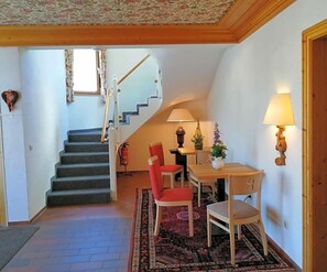 A staircase leading to a second floor, a dining area with a table and chairs, and a lamp on the wall. - Landhotel Reckenberg (Stegen)