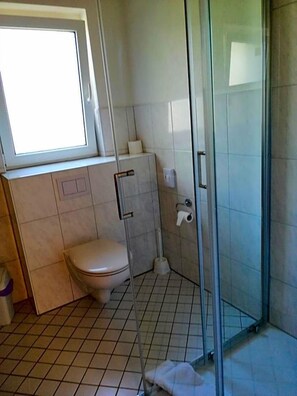 A bathroom with a toilet, a shower enclosure, and a window. - Landhotel Reckenberg (Stegen)