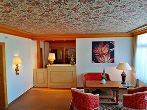 A hotel room with a floral ceiling, a dining area with a table and chairs, and a large painting on the wall. - Landhotel Reckenberg (Stegen)