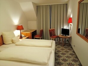 A hotel room with a bed, a desk, a chair, a television, and a mirror. - Landhotel Reckenberg (Stegen)