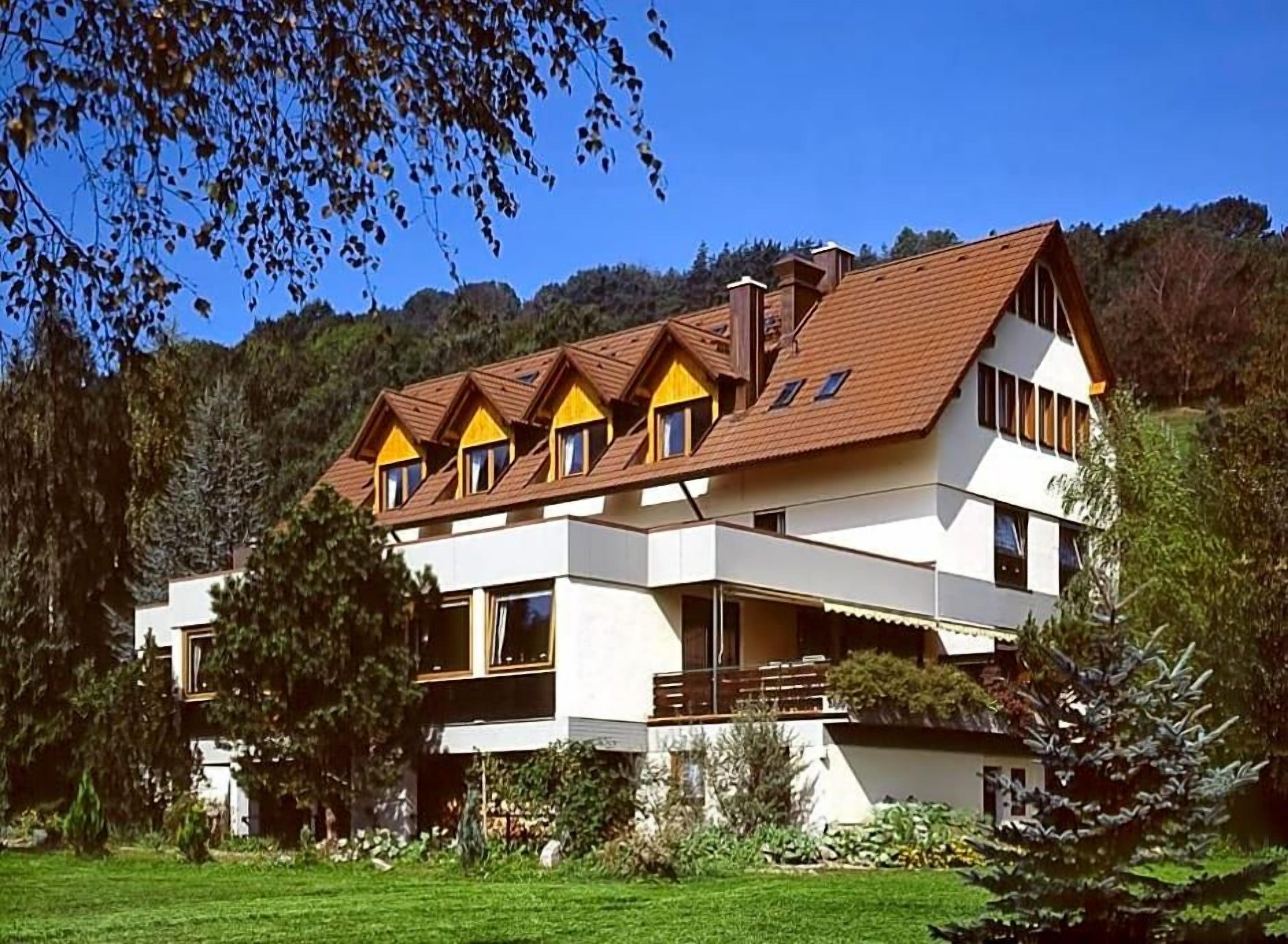 A multi-story building with a sloped roof, surrounded by greenery and trees.