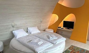 A modern bedroom with a bed, bedside tables, a television, and a unique architectural design.