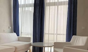 A room with a white sofa, a round table, and a window with blue curtains.