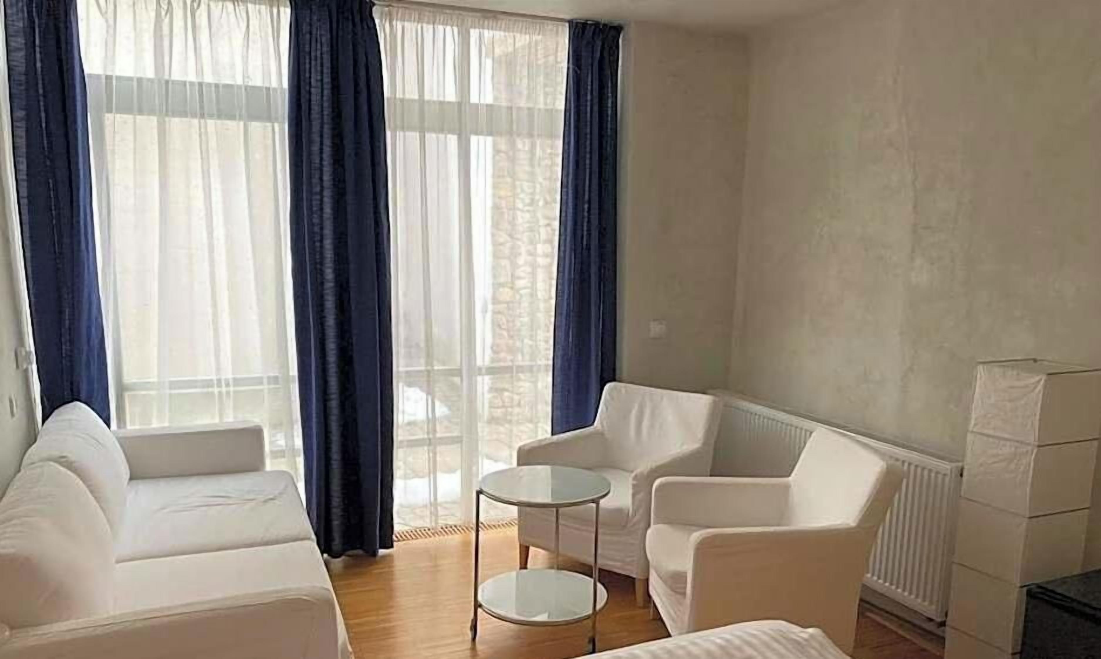 Una habitación con un sofá blanco, dos sillones, una mesita redonda y un radiador.