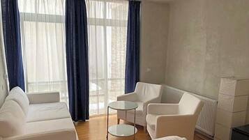 Una habitación con un sofá blanco, dos sillones, una mesita redonda y un radiador.