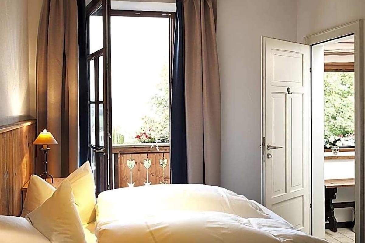 A bedroom with a bed, curtains, a window, and a door.