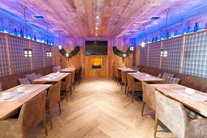 Restaurante com paredes de madeira, chão em padrão espinha de peixe e mesas com cadeiras.