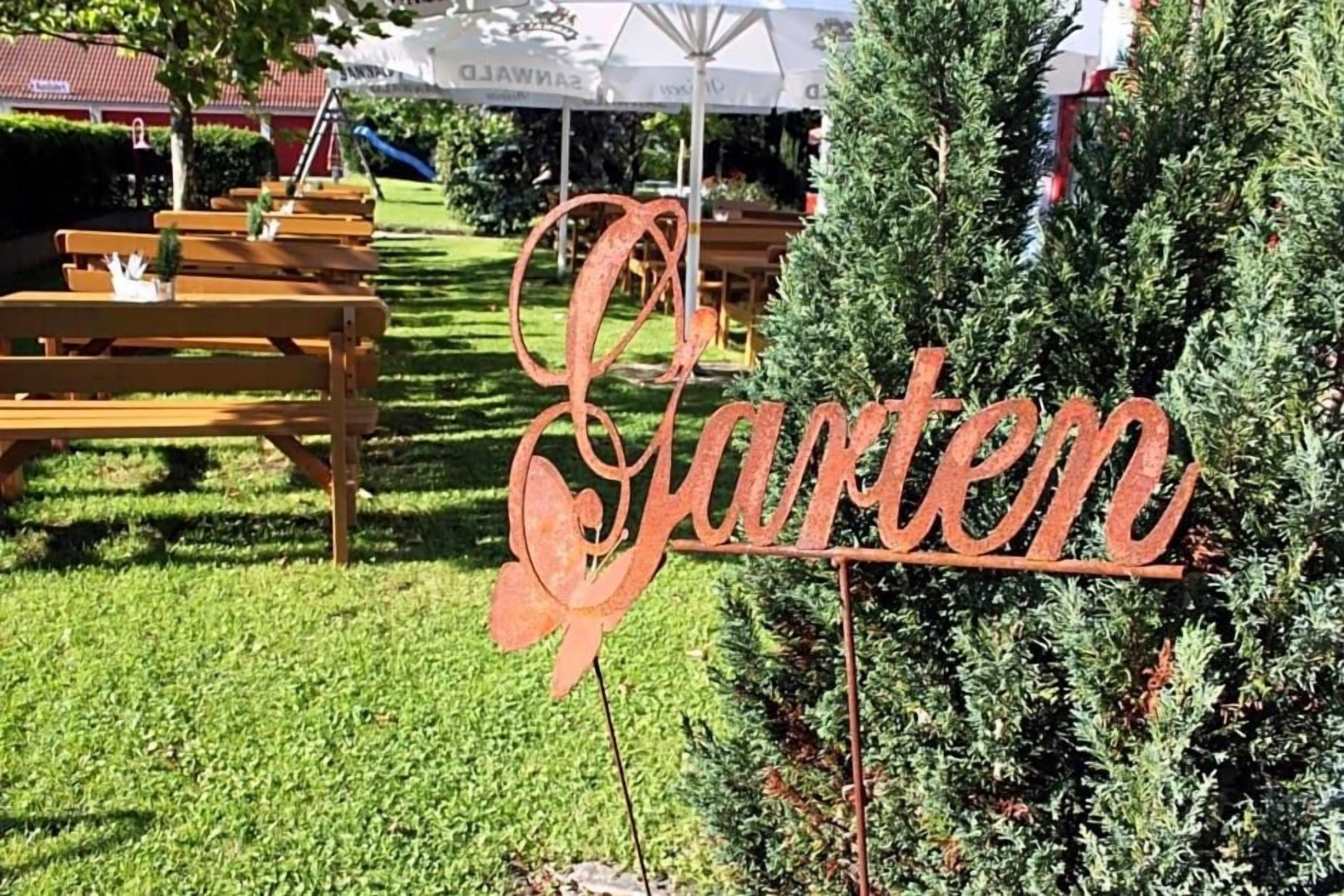 A metal sign with the word 'Garden' in cursive, placed in a grassy area with wooden benches and a small tree.