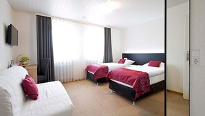 Une chambre d’hôtel avec deux lits, un canapé, une télévision et un bureau avec une lampe.