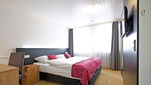 Une chambre d’hôtel équipée d’un lit, d’un bureau, d’une chaise, d’une télévision et d’une fenêtre avec des rideaux.