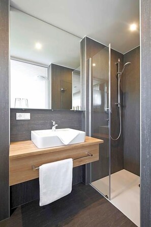 A modern bathroom with a glass-enclosed shower, a white sink, and a wooden vanity. - Landgasthof Lamm (Aalen)