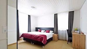Une chambre d’hôtel avec un lit, un bureau, une chaise et une fenêtre avec des rideaux.
