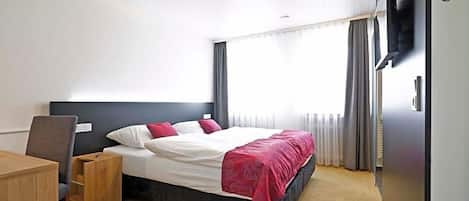 A hotel room with a bed, a desk, a chair, a television, and a window with curtains.