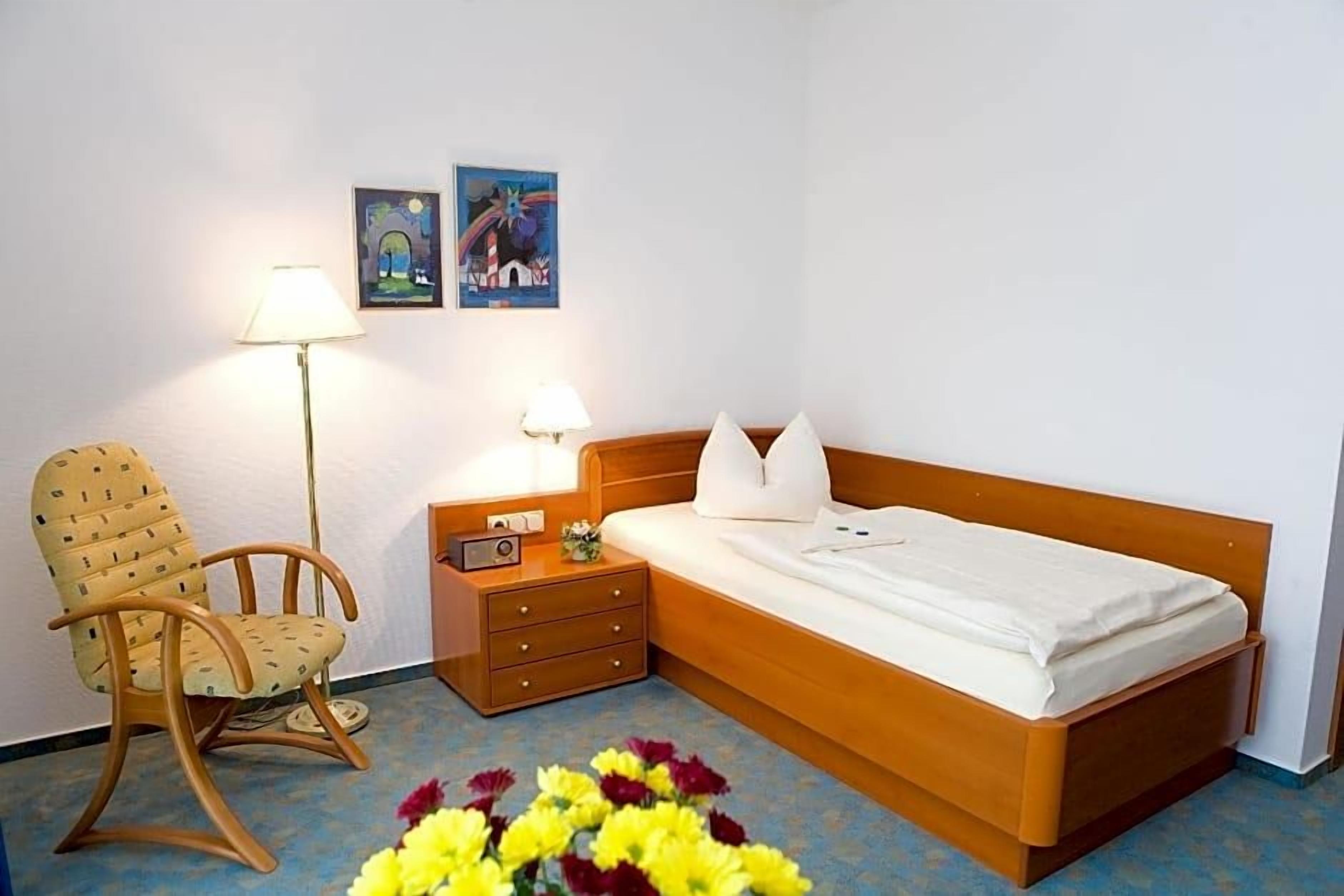 A hotel room with a wooden bed, a chair, a nightstand, and a lamp.