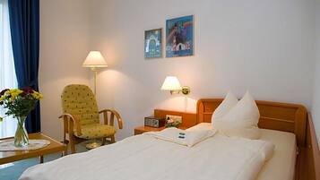 A hotel room with a bed, two lamps, a chair, a table with a vase of flowers, and two wall art pieces.