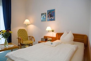 A hotel room with a bed, two lamps, a chair, a table with a vase of flowers, and two wall art pieces.